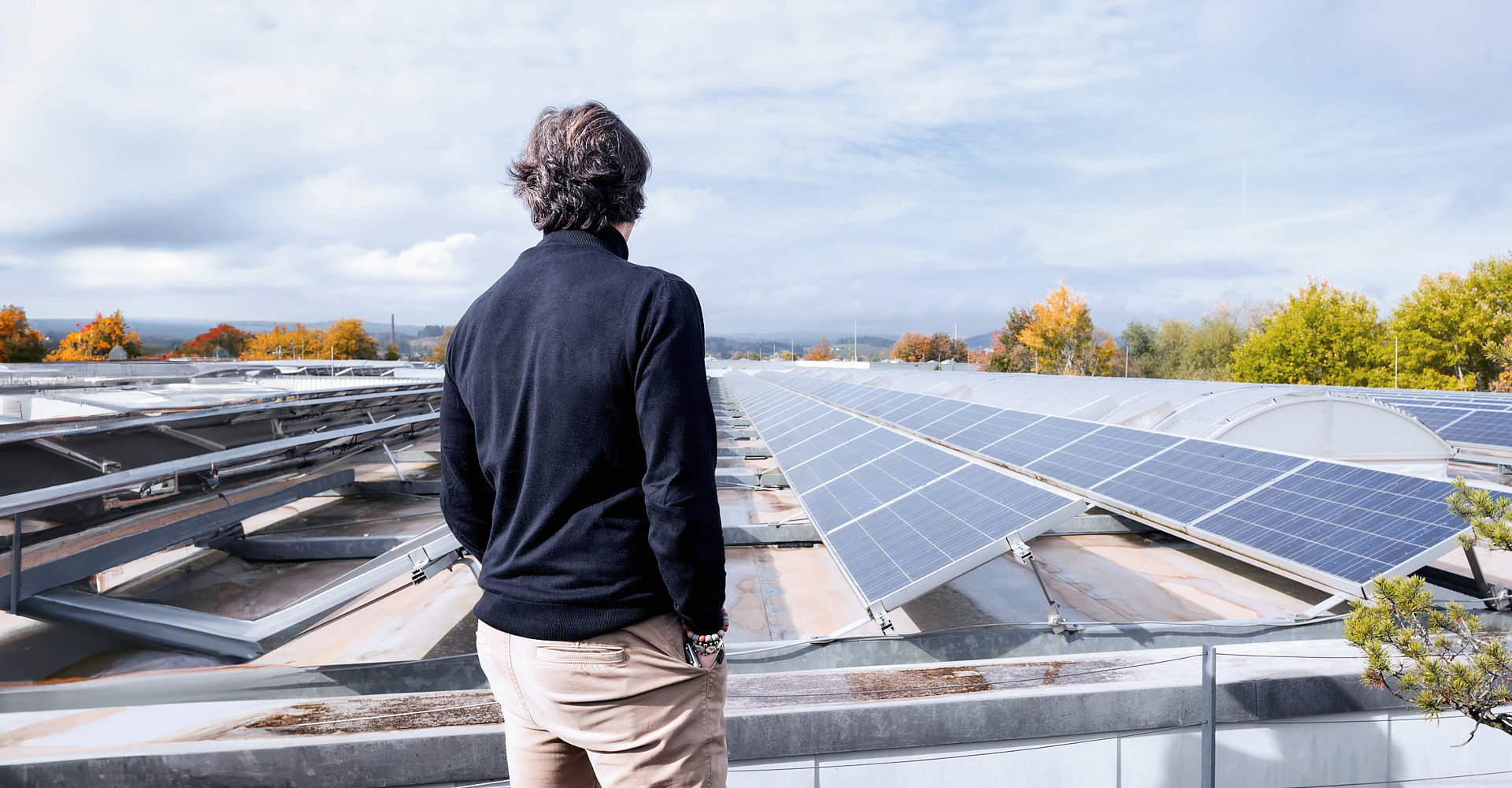 Mitarbeiter schaut über die Dächer einer Firma die voller Photovoltaik-Anlagen ist.