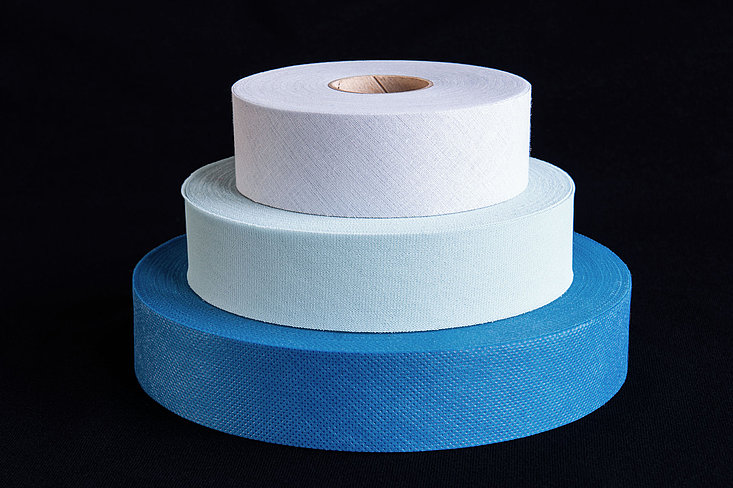 Stapel aus drei Rollen Textilbändern in grau, pastellgrün und blau.