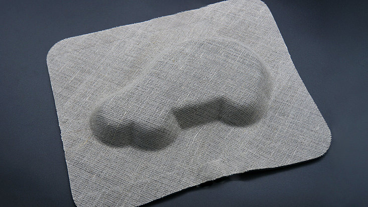 Viereckiges mit Leinengewebe bespanntes Formbauteil in das die Silhouette eines Autos eingeprägt ist.
