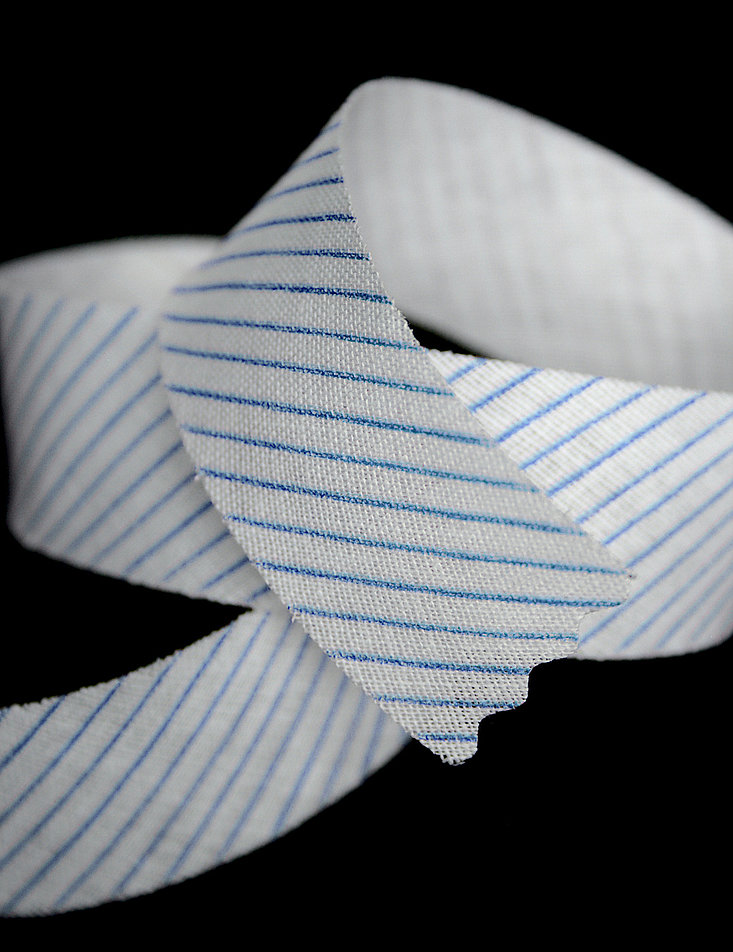 Lose übereinandergelegtes Band aus Schräggewebe mit bedruckten schrägen blauen Streifen.