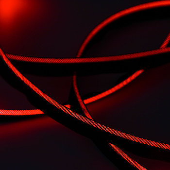 Von einem löchrigen schwarzen Textil umhüllter Lichtleiter, der durch die Löcher rot Leuchtet.